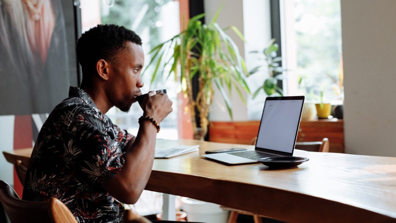 Black man drinking coffee at a laptop